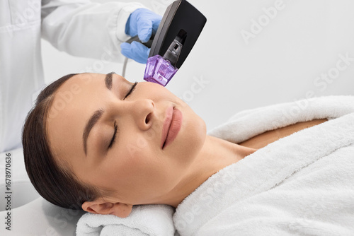 Woman while RF lifting procedure for her face skin tightening with cosmetologist at a beauty salon
