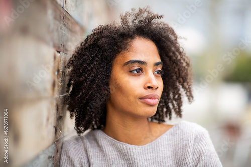 Thoughtful Woman Leaning Against Wall Outdoors Looking Away