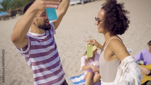 Group of friends having fun at a beach day party. They are dancing, laughing, and drinking cocktails under the sun.