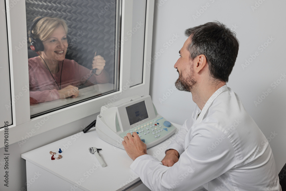 Obraz premium Audiological exam. Audiologist doing hearing check-up to mature woman in soundproof audiometric booth. Hearing loss treatment