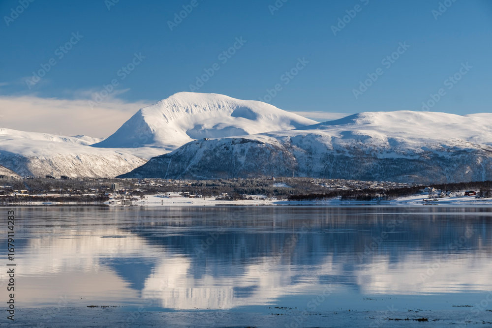 Obraz premium Snow covered coast of Norwegian fjord near Troms at Christmas time. A sunny winter day in Northern Norway above the Arctic Circle
