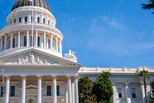 The California State Capitol building in Sacramento features neoclassical architecture, a dome with a flagpole, white columns, and surrounding greenery.