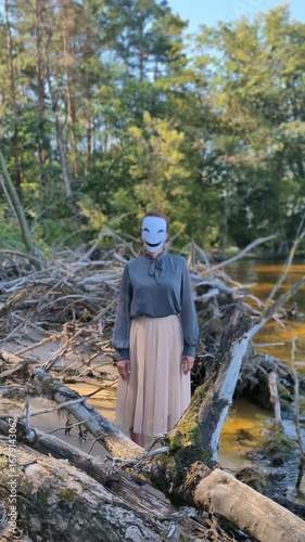 Animegao mask hanging on tree near water, mysterious atmosphere.