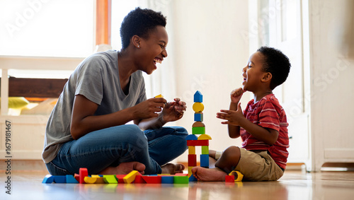 Photo of a mother and her young son laugh together while playing with colorful building blocks on the floor