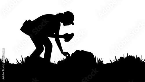 Silhouette of a person examining a rock with a magnifying glass in a grassy field landscape view