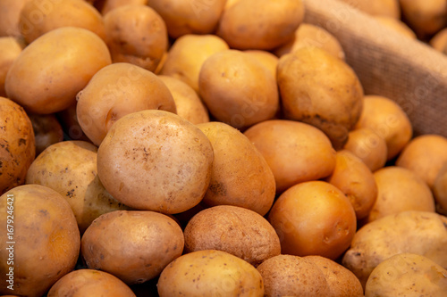 Lots of raw potatoes lying in a tray on the display case of a vegetable shop. Natural not perfect many potatoes. Close-up