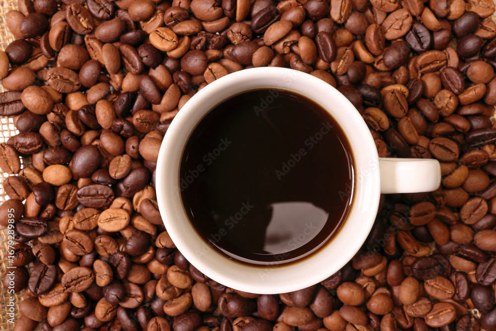 Fototapeta premium Fresh roasted aromatic arabica coffee bean smoking steaming white ceramic cup black drink on rustic jute fabric mat