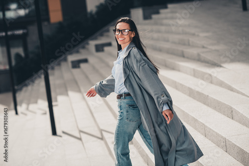 Stylish young woman in gray coat enjoying an urban city walk during spring day with vibrant and charming energy