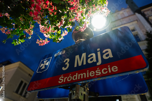 Fotografie Street 3 Maja sign under lamp with flowers in Rzeszow, Poland during evening