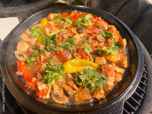 Beef meat and vegetables stew in black bowl with roasted baby potatoes. Dark background grill kamado.