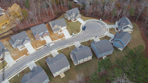 Residential cul-de-sac street with completed homes, adjacent timber-framed builds, bordered by tall trees forming natural buffer between developed lots and ongoing construction activity, Atlanta