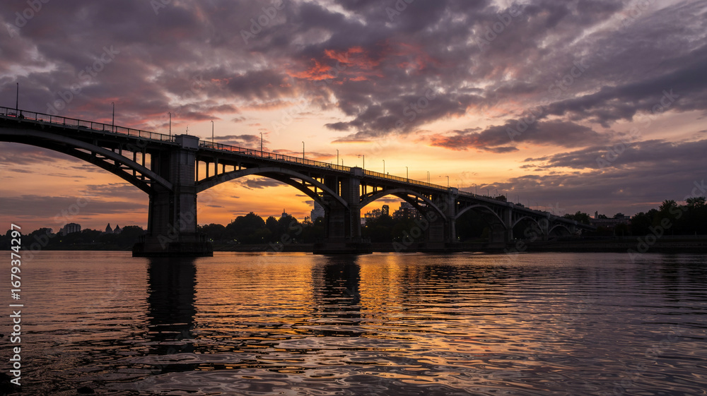 Fototapeta premium A bridge’s arches stand dark against the colorful sk
