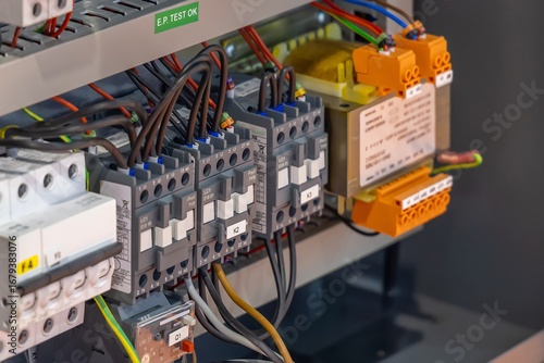 Close-up of an industrial electrical control panel featuring circuit breakers, relays, and wiring connections in a metallic enclosure. Electrical engineering concept