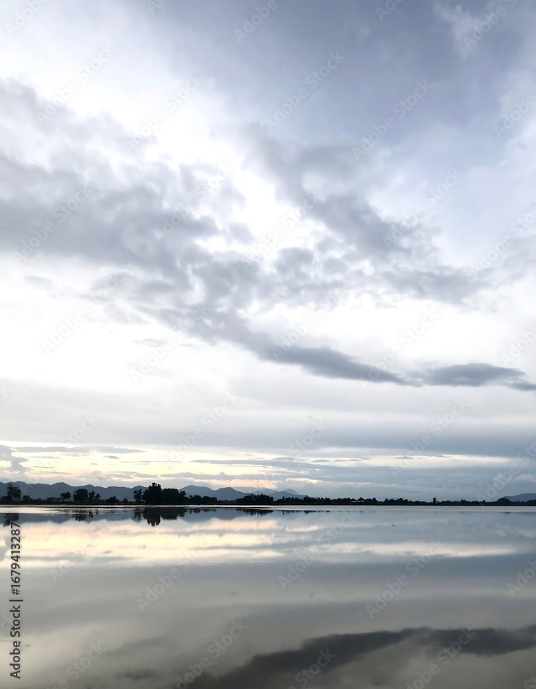 Obraz premium A tranquil landscape showcases a calm body of water reflecting a soft, overcast sky.