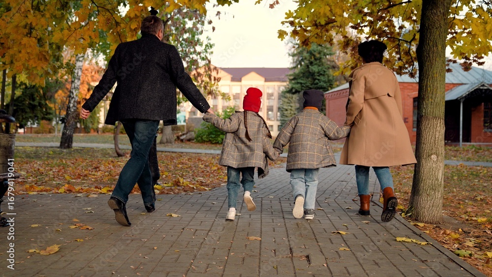 Fototapeta premium Happy family, children play, run, holding hands of mom, dad, in autumn park. Kids, mom, dad play together, holding hands in autumn outdoors. Family weekend walk, mother, child, father in park. People