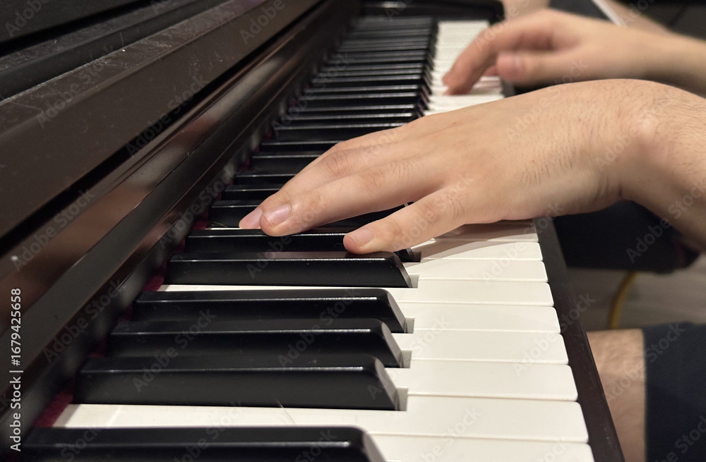Fototapeta premium Close-up view of hands playing piano keys, showcasing the elegant black and white keys, highlighting musical expression and the art of performance in a cozy environment