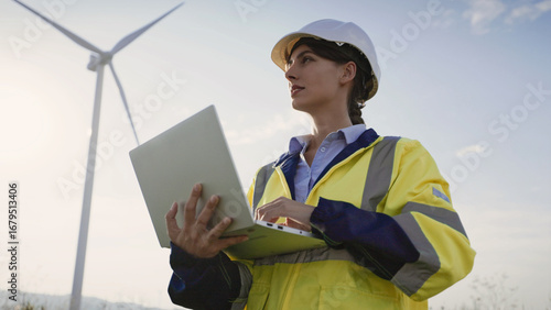 Wallpaper Mural Cute Caucasian girl standing in front of working wind turbine. Entering information on laptop with one hand. Pressing keys on keyboard. Recording her observations as maintenance inspector. Torontodigital.ca