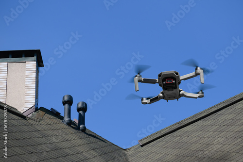 Drone in the air inspecting the roof over the house closeup on blue sky background