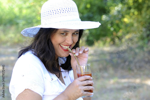 Frau trinkt mit Strohhalm Tomatensaft. / Woman drinking tomato juice with straw.