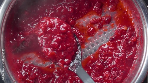 A spoon scoops thick, homemade cranberry sauce from a saucepan. This sweet and tart condiment is the perfect topping for classic Swedish meatballs. A close-up of the cooking process