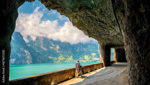 A 55-year-old man stops in a tunnel in Switzerland and admires, through rock windows, the magnificent scenery of the shores of Lake Lucerne and the mountains during his bike ride on holiday.