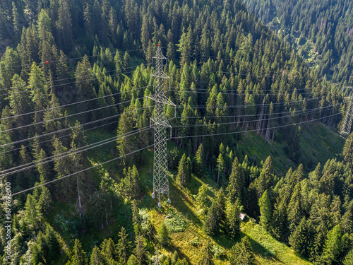 Aerial view of power line pylon in alpine forest in Switzerland. Electric current distribution with power grid.