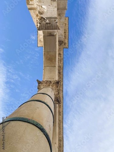 Low-angle view of an ancient stone column with intricate Corinthian capital details, reaching toward a vibrant blue sky. Historic architecture symbolizing strength, culture, and timeless design.