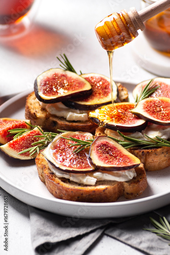 Delicious fig and honey toast topped with creamy cheese and fresh rosemary, beautifully arranged on a white plate, showcasing a gourmet culinary experience