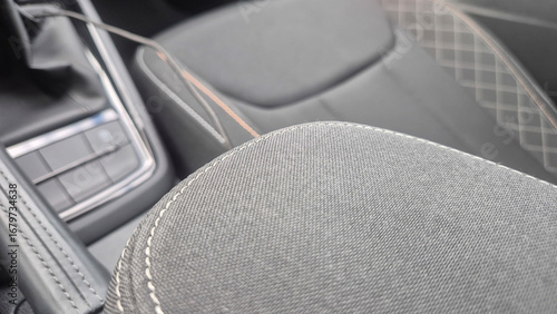 Close-up view of a car interior featuring a textured black fabric seat with white stitching, showcasing modern design elements and luxury details in an automobile.