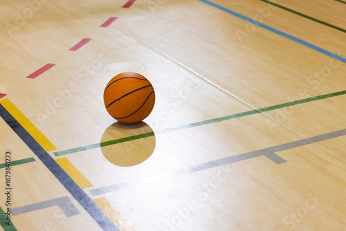 Orange basketball resting on polished gym floor with green yellow dark blue, red court lines