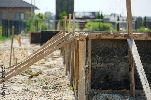 Construction site shows wooden formwork ready for concrete pouring on a sunny day in a residential area