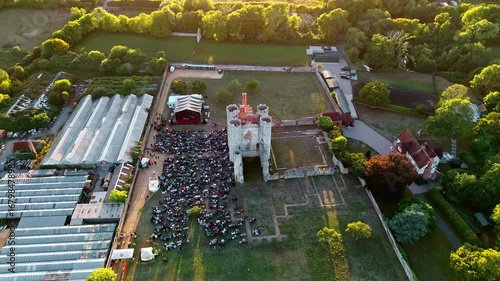 aerial high wide angle drone shot side on view flying over panning down tacking ancient old English Titchfield abbey in countryside with large crowd of people at sunset in summer