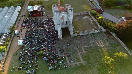 aerial side on drone shot flying over panning down on ancient old English Titchfield abbey ruins in countryside with large crowd of people in countryside at sunset in summer