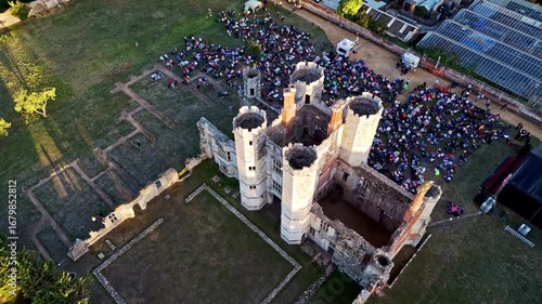 aerial high angle close up drone shot panning right over ancient old English Titchfield abbey ruins in countryside with large crowd of people in summer at sunset