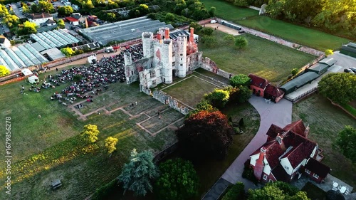 aerial mid angle wide drone shot of ancient old English Titchfield abbey ruins with large crowd of people in countryside panning left in summer at sunset