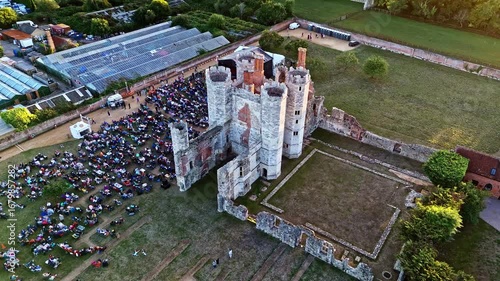 aerial wide angle drone shot moving down panning up of ancient English Titchfield abbey ruins with large crowd of people at sunset in summer
