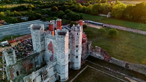 aerial drone shot quickly flying forward and left over ancient English Titchfield abbey ruins with large crowd of people in countryside in summer at sunset