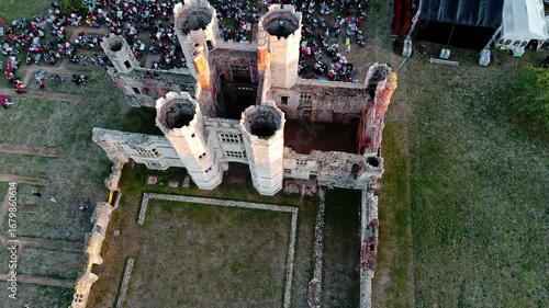 aerial Birds Eye drone shot over ancient English Titchfield abbey moving right with large crowd of people gathered in summer at sunset