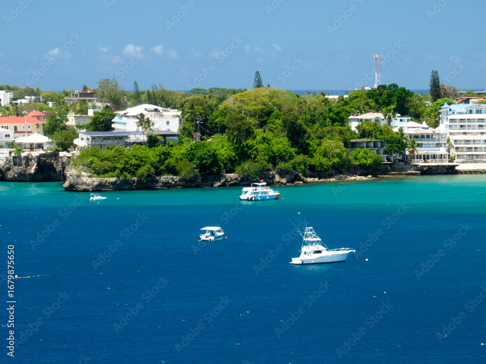 Obraz premium A long, sandy beach stretching along the coast, lined with lush green forest and resort-like buildings further away. A wide, stunning bay with vibrant blue and turquoise water, where several boats are