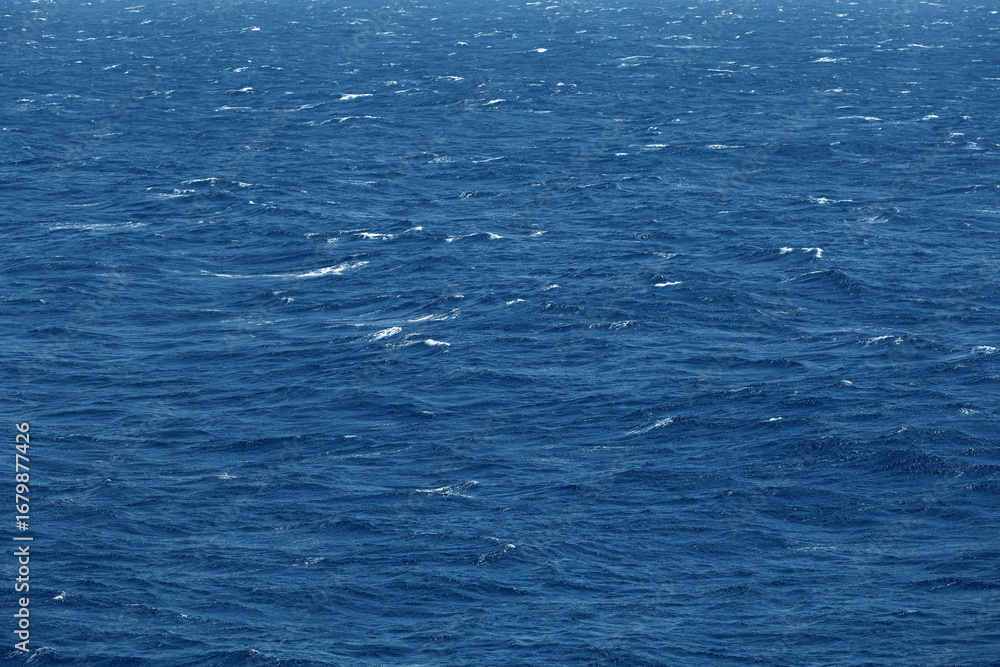 Fototapeta premium Sea surface aerial view. Background shot of clear sea water surface. Blue sea water in calm. Sea texture. Background blue waves of the sea with sea foam.