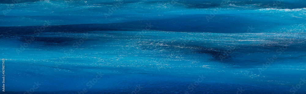 Fototapeta premium Sea surface aerial view. Background shot of clear sea water surface. Blue sea water in calm. Sea texture. Background blue waves of the sea with sea foam.