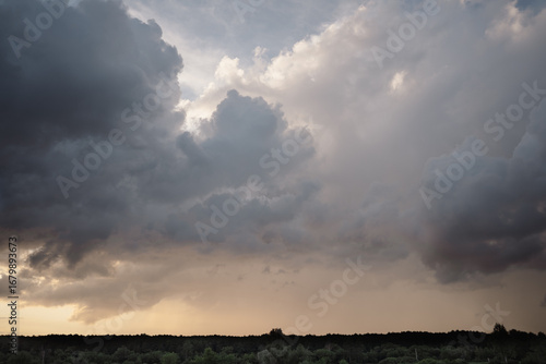 Dramatic thunderous sunset sky with dark huge rain clouds over green forest