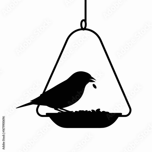 Silhouette of a small bird eating seeds from a hanging bird feeder