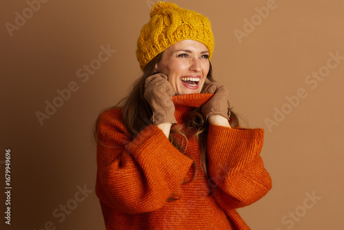 Billede på lærred A cheerful woman with light brown hair laughs heartily, adjusting her chunky orange turtleneck and yellow cable-knit beanie, radiating warmth and joy