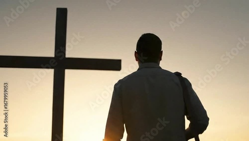 A man in silhouette stands before a large wooden cross against a warm sunset sky - believer release Jesus Christianity new modern
