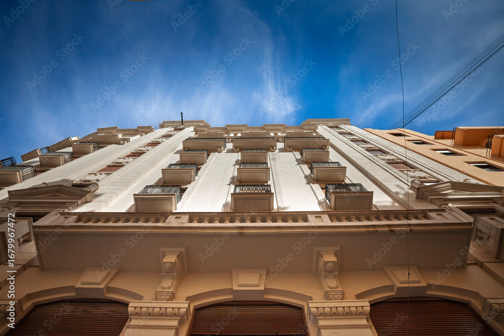 Obraz premium Upward view of a residential facade in Valencia old town, showing balconies, classical details and small terraces. The composition emphasizes housing and property character in the historic center.