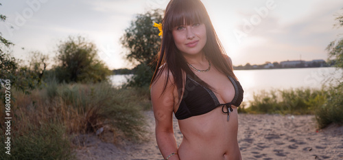 Young woman in black bikini smiling at sunset on beach with natural scenery