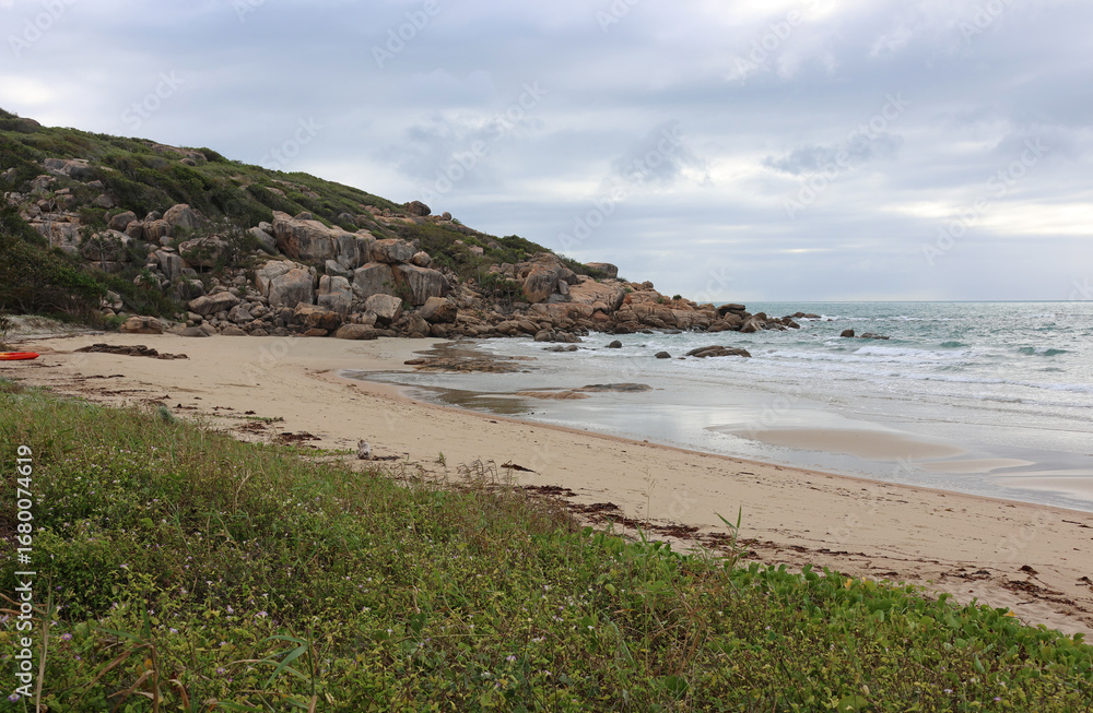 Obraz premium Peaceful beach with sand, gentle waves, vegetation and a rocky cliff at Rose Bay beach near Bowen in Queensland, Australia