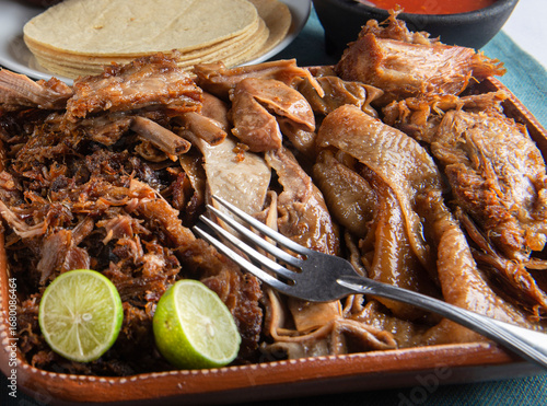 Traditional dish from central and southern Mexico called CARNITAS with a fork on top and lemon slices corn tortillas in the background macro photography