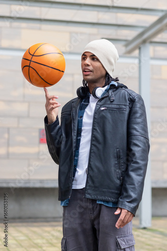 African american man spinning orange basketball on fingertip in lawn with white beanie